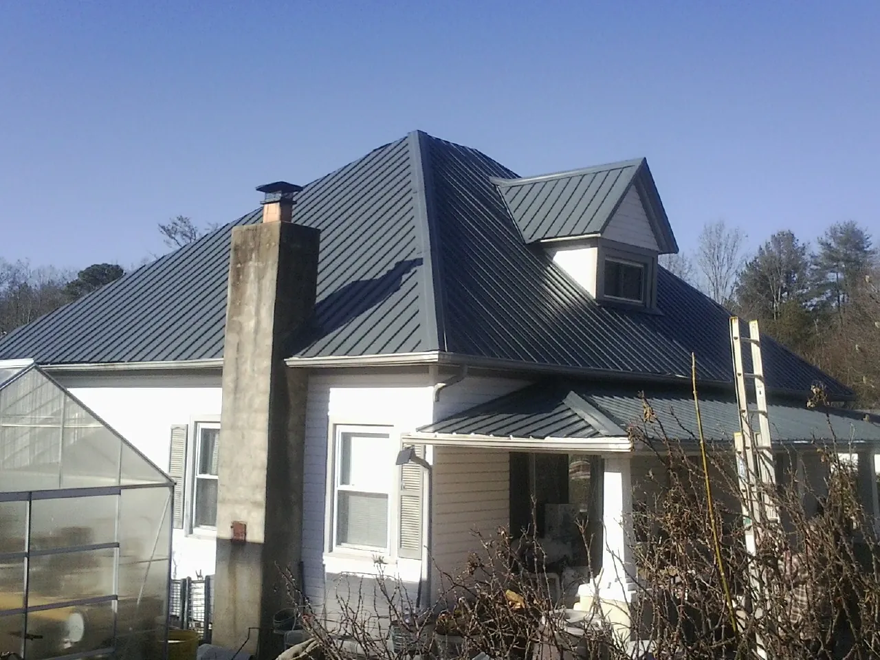 Dark blue standing seam metal roof on a white farmhouse with dormer — Slate & Tile Roof Repair by Roofing Brothers in Cherryville