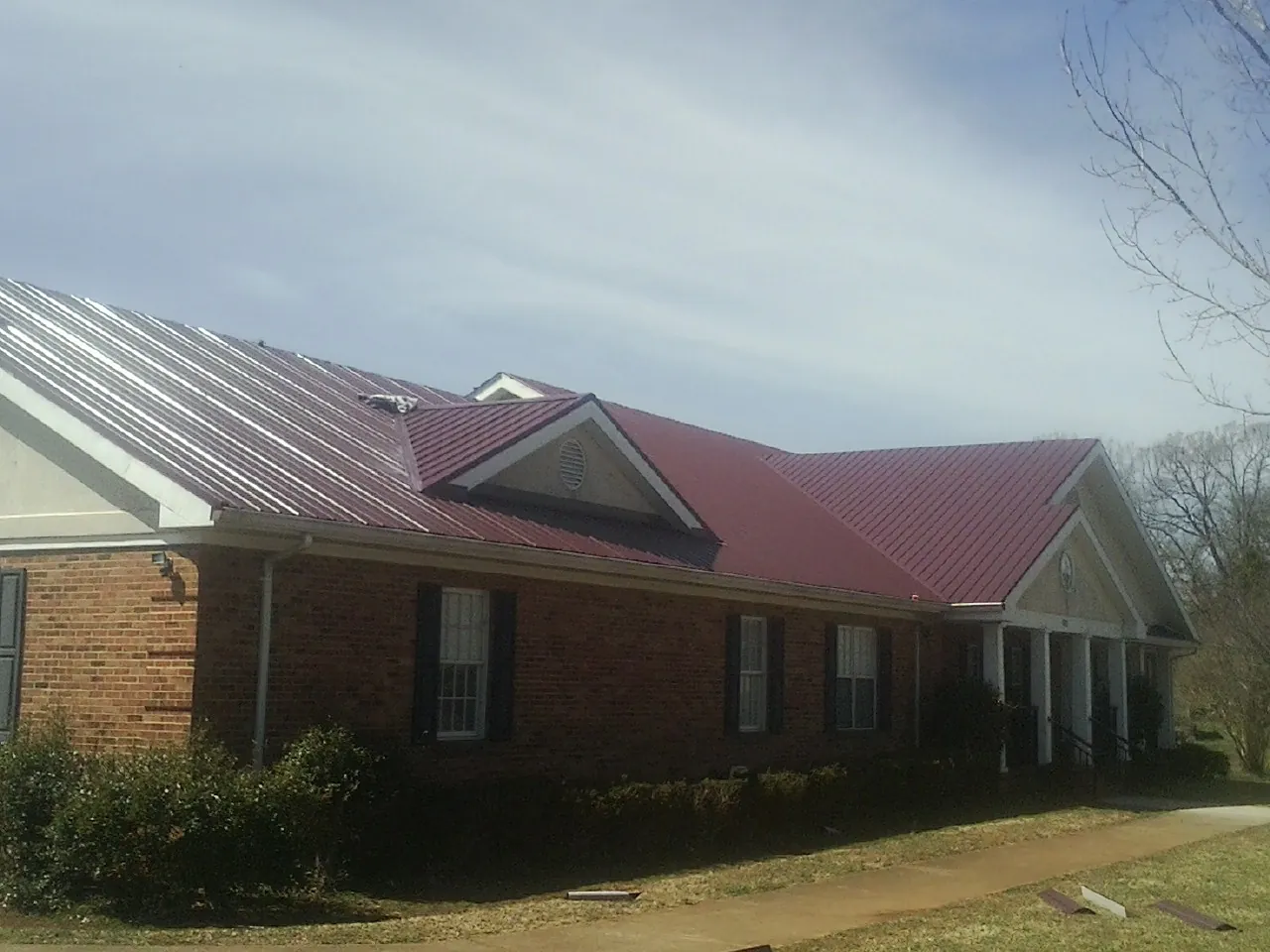 Red metal roof with gabled entries on a long brick building, from a Hail Damage Roof Repair job in Cherryville