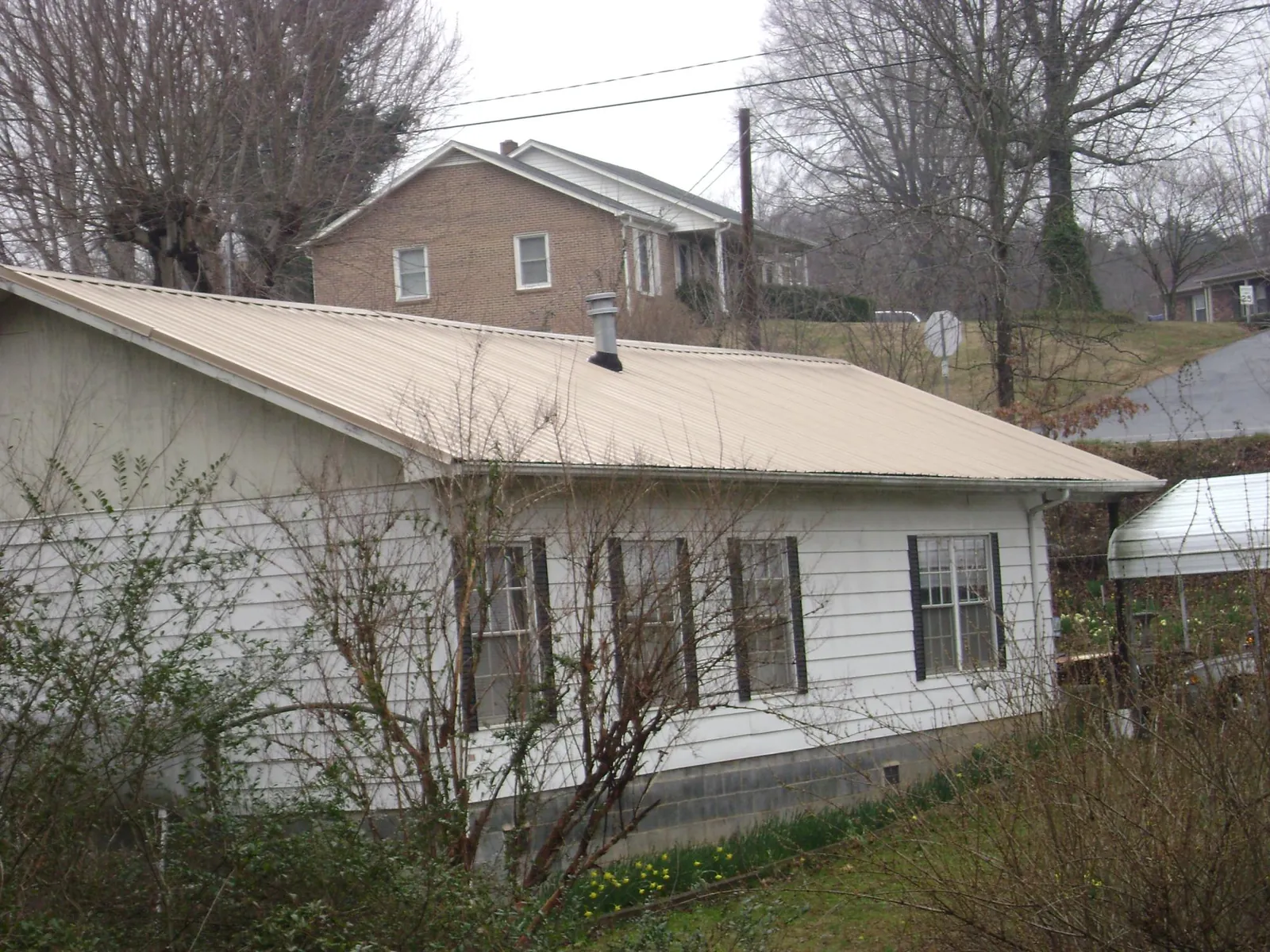 Tan metal roof on a white sided house set into a hillside — Commercial Roofing by Roofing Brothers in Cherryville